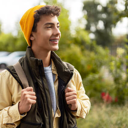 Smiling teenage boy with braces wearing a yellow beanie outdoors
