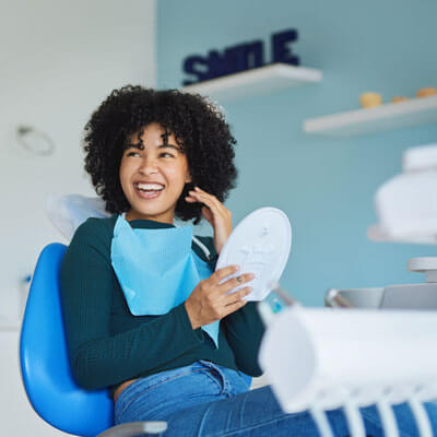 Smiling patient in the dental chair holding a mirror